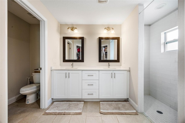 bathroom with tile patterned flooring, vanity, toilet, and a tile shower