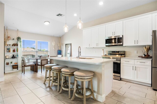 kitchen with a center island with sink, white cabinets, sink, hanging light fixtures, and appliances with stainless steel finishes