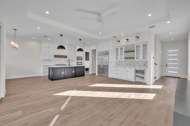 kitchen featuring white cabinets, wine cooler, a kitchen island with sink, decorative light fixtures, and stainless steel appliances