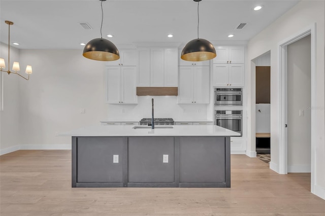 kitchen with hanging light fixtures, light hardwood / wood-style floors, an island with sink, white cabinets, and stainless steel double oven