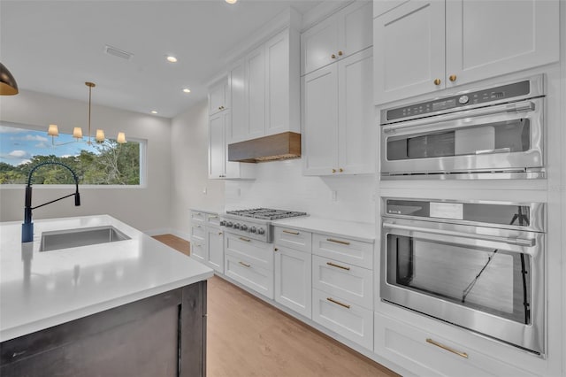 kitchen with sink, decorative light fixtures, white cabinetry, stainless steel appliances, and a notable chandelier