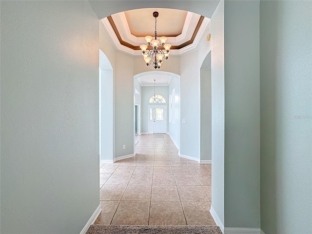 hall with crown molding, an inviting chandelier, a tray ceiling, and light tile patterned flooring