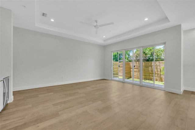 unfurnished room with baseboards, visible vents, a raised ceiling, a ceiling fan, and light wood-type flooring