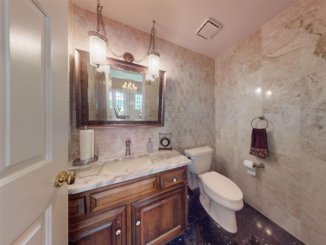 bathroom featuring vanity, toilet, tile walls, and a notable chandelier