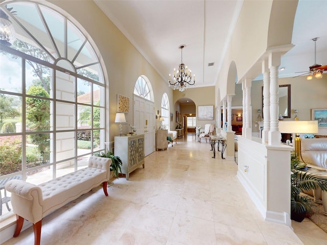 foyer with ceiling fan with notable chandelier, ornamental molding, decorative columns, and a towering ceiling