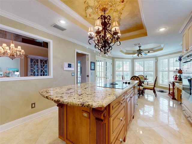 kitchen with crown molding, black electric cooktop, a tray ceiling, a kitchen island, and ceiling fan with notable chandelier