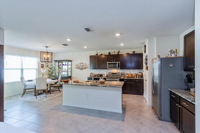 kitchen with appliances with stainless steel finishes, light tile patterned floors, light stone countertops, and a center island with sink