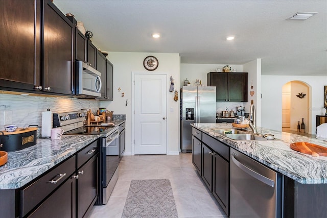 kitchen with stainless steel appliances, sink, an island with sink, light tile patterned flooring, and tasteful backsplash