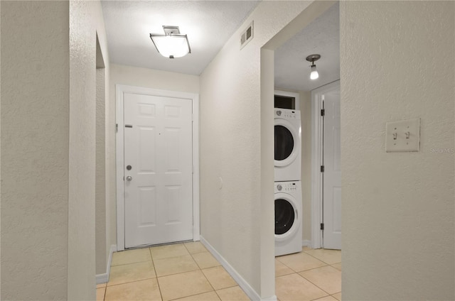 washroom featuring a textured ceiling, stacked washer / dryer, and light tile patterned flooring