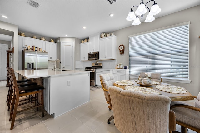 kitchen featuring an inviting chandelier, sink, hanging light fixtures, appliances with stainless steel finishes, and a center island with sink