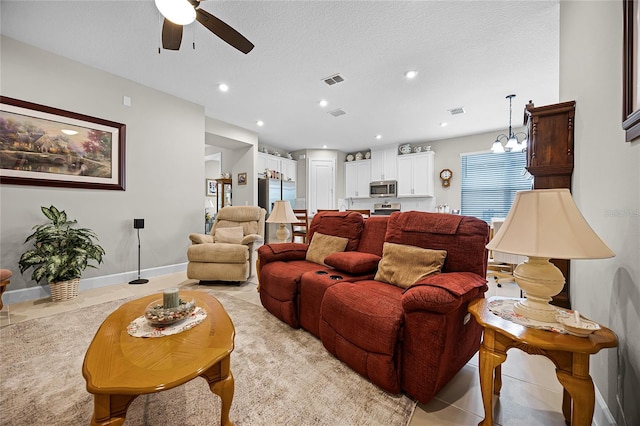 tiled living room with a textured ceiling and ceiling fan with notable chandelier