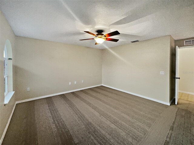 empty room featuring a textured ceiling, dark carpet, and ceiling fan