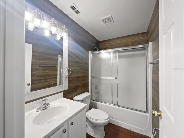 full bathroom featuring toilet, vanity, a textured ceiling, wood walls, and enclosed tub / shower combo