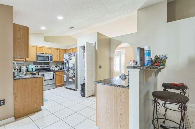 kitchen featuring a breakfast bar, stainless steel appliances, kitchen peninsula, lofted ceiling, and dark stone countertops