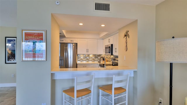 kitchen featuring white cabinets, backsplash, stainless steel appliances, kitchen peninsula, and a breakfast bar