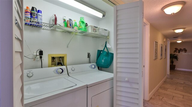 laundry room with separate washer and dryer, light wood-type flooring, and a textured ceiling