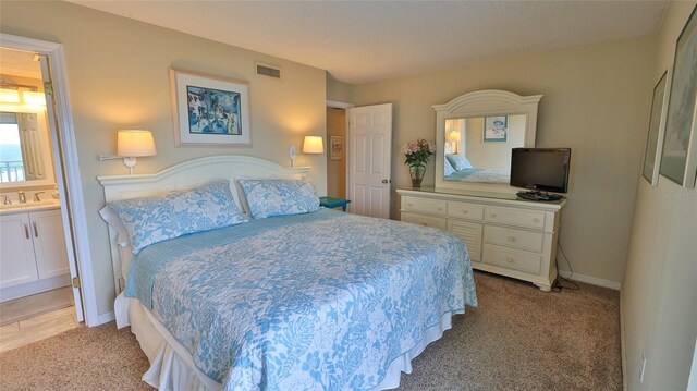 bedroom with ensuite bathroom, light carpet, and sink