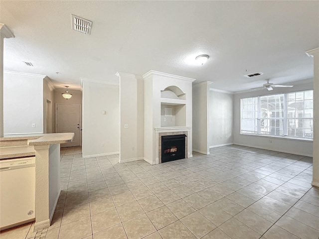 unfurnished living room with a tiled fireplace, built in shelves, crown molding, ceiling fan, and light tile patterned flooring