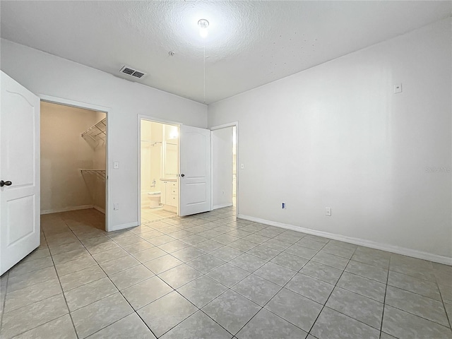 unfurnished bedroom featuring a textured ceiling, a walk in closet, a closet, and light tile patterned floors