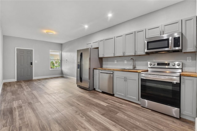 kitchen with stainless steel appliances, sink, wooden counters, and light hardwood / wood-style floors