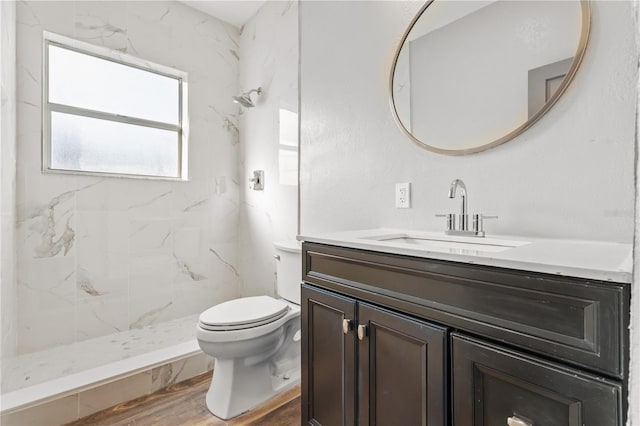 bathroom featuring wood-type flooring, toilet, a tile shower, and vanity