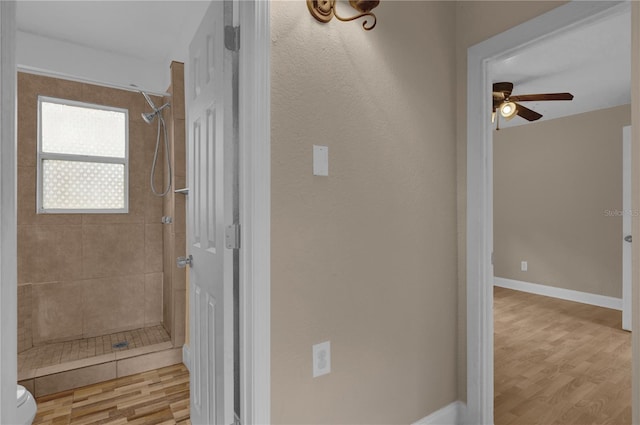 bathroom featuring wood-type flooring, toilet, a tile shower, and ceiling fan