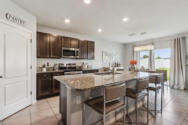 kitchen featuring stone countertops, appliances with stainless steel finishes, a kitchen island with sink, a kitchen bar, and sink