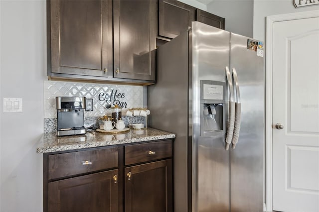 kitchen with light stone countertops, dark brown cabinets, stainless steel fridge with ice dispenser, and decorative backsplash