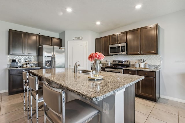 kitchen with a kitchen breakfast bar, light stone countertops, a center island with sink, stainless steel appliances, and sink