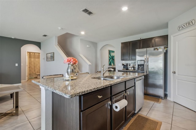 kitchen featuring light stone countertops, light tile patterned floors, appliances with stainless steel finishes, a kitchen island with sink, and sink