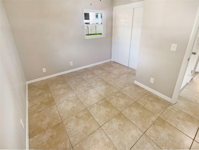 unfurnished bedroom featuring light tile patterned flooring, baseboards, and a closet