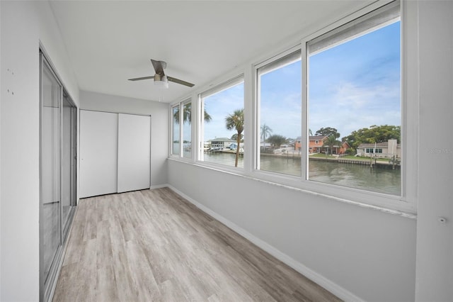 unfurnished sunroom with ceiling fan and a water view