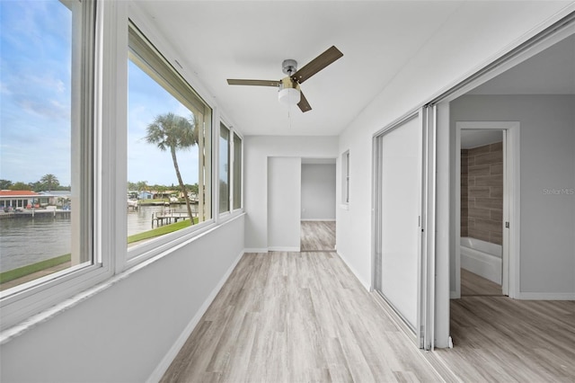 unfurnished sunroom featuring ceiling fan and a water view