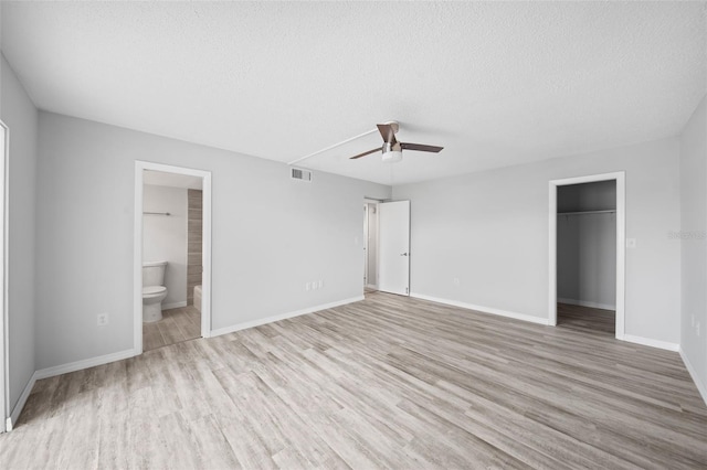 unfurnished bedroom with light wood-type flooring, ceiling fan, connected bathroom, and a textured ceiling