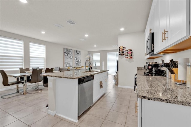 kitchen with a center island with sink, stainless steel appliances, sink, light stone counters, and white cabinets