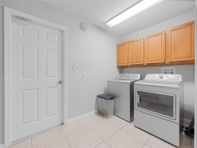 clothes washing area with light tile patterned floors, a textured ceiling, separate washer and dryer, baseboards, and cabinet space