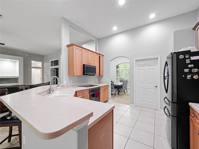 kitchen with light tile patterned floors, a breakfast bar area, a peninsula, a sink, and black appliances