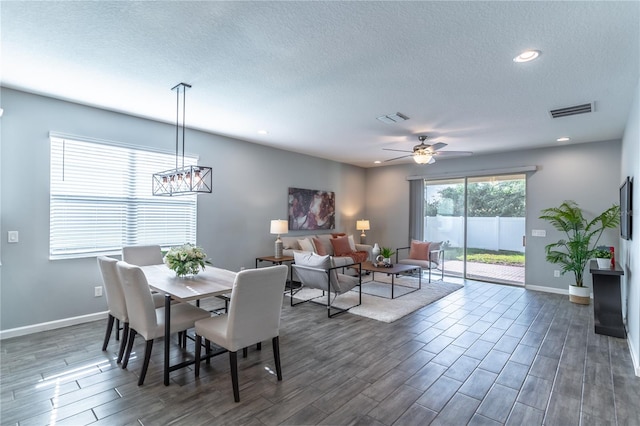 dining area featuring ceiling fan with notable chandelier, dark wood-type flooring, and a textured ceiling