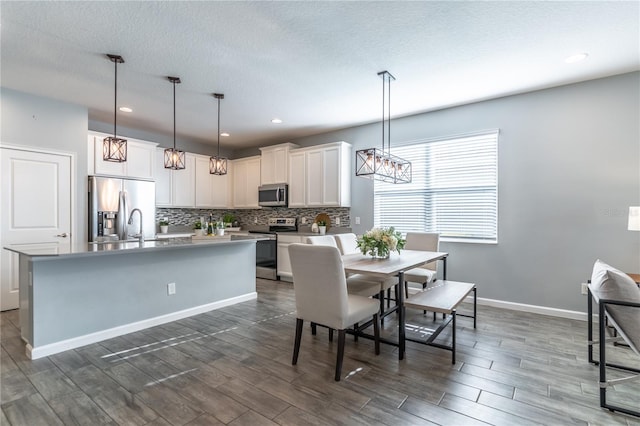 interior space featuring a textured ceiling, dark hardwood / wood-style floors, a center island with sink, pendant lighting, and appliances with stainless steel finishes