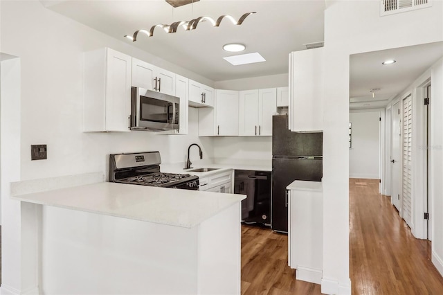 kitchen with visible vents, light wood finished floors, a sink, black appliances, and light countertops