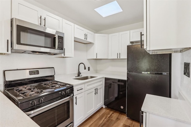 kitchen featuring a sink, wood finished floors, black appliances, and white cabinets