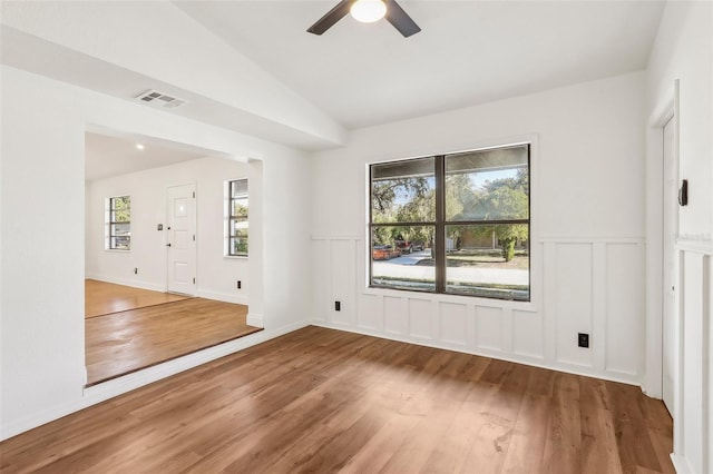 unfurnished bedroom featuring a wainscoted wall, lofted ceiling, wood finished floors, and visible vents