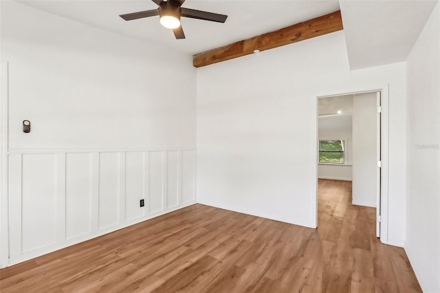 unfurnished room with beamed ceiling, light wood-style floors, a wainscoted wall, and a ceiling fan