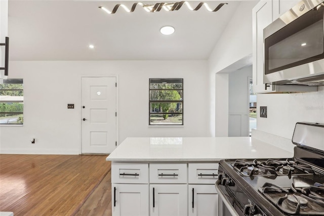 kitchen with stainless steel microwave, range with gas cooktop, a peninsula, white cabinets, and light countertops