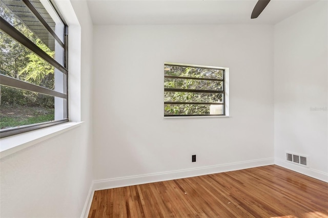 empty room with visible vents, a ceiling fan, baseboards, and wood finished floors