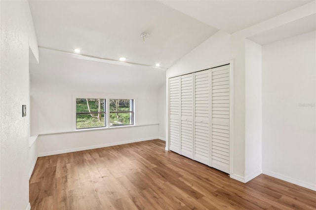 unfurnished bedroom featuring wood finished floors, baseboards, lofted ceiling, recessed lighting, and a closet