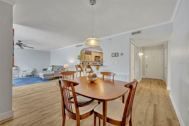 dining area with ceiling fan, ornamental molding, a textured ceiling, and light wood-type flooring