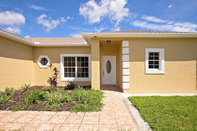 doorway to property with roof with shingles and stucco siding