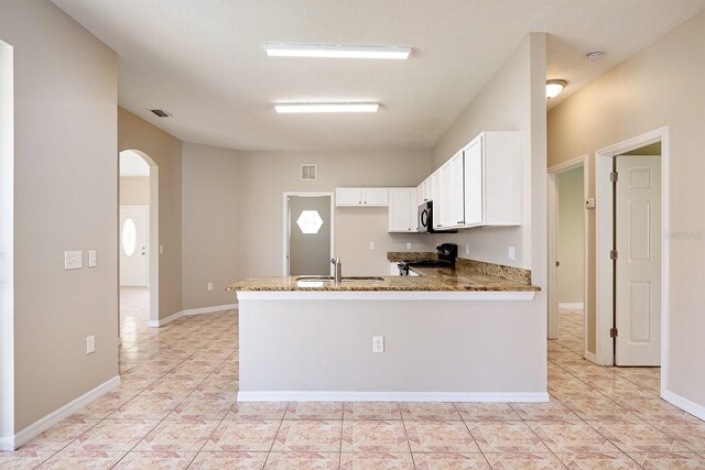 kitchen featuring arched walkways, stone countertops, stove, a sink, and white cabinets