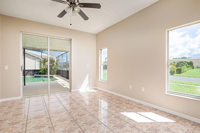 spare room with a textured ceiling, light tile patterned floors, a ceiling fan, a sunroom, and baseboards